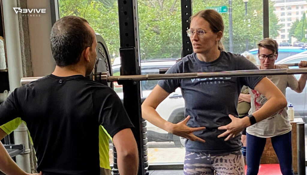 A coach instructing a member on how to use their core for squatting.